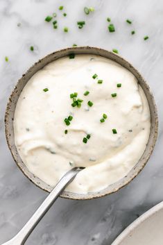 a bowl filled with white sauce and chopped green onions