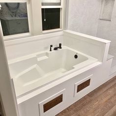 a white bath tub sitting under a window next to a wooden flooring area in a bathroom