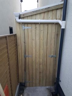 a wooden gate is open in the corner of a small backyard area with concrete flooring