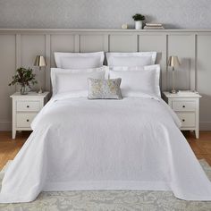 a bed with white linens and pillows in a small room next to two nightstands