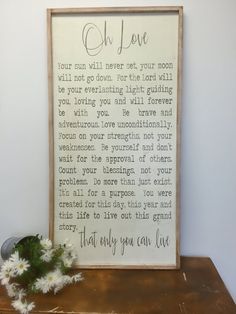 a wooden framed sign that says oh love with daisies on a table next to it