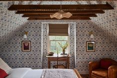 a bedroom with blue and white wallpaper has a bed, chair, desk and window