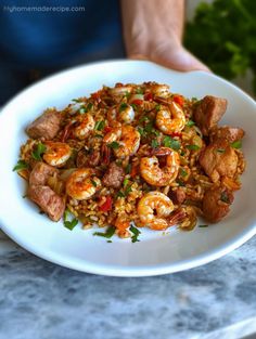 a white plate topped with shrimp and rice next to a person's hand holding it