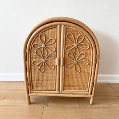 a wicker cabinet with an intricate design on the front and side doors, sitting on a hard wood floor