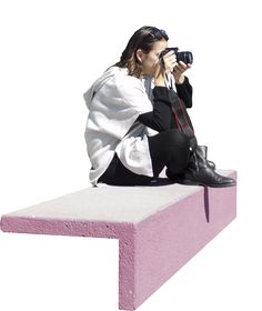 a woman sitting on top of a pink bench holding a camera up to her face