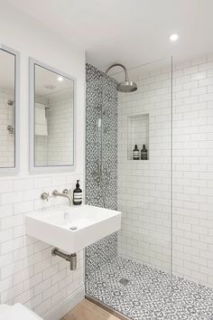 a white bathroom with black and white tile on the floor, shower stall, and sink