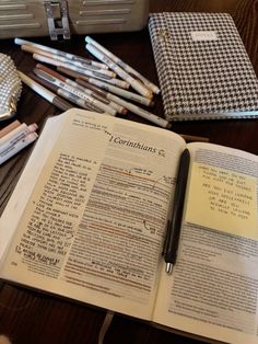 an open book with writing on it next to several pens and pencils in case