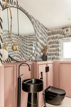 a bathroom with pink and black walls, a round mirror over the toilet and a sink