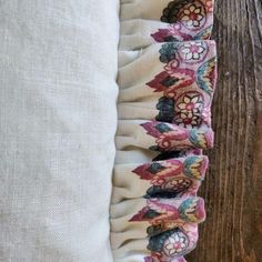 the back of a pillow with ruffles and flowers on it, against a wooden background