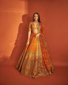 a woman in an orange and gold lehenga is standing against a red wall