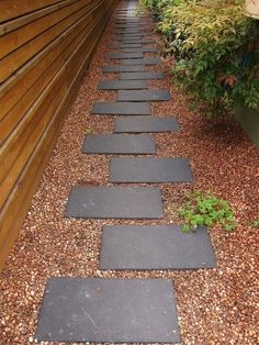 a walkway made out of stone in front of a wooden wall and plants on the side