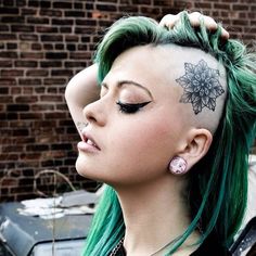 a woman with green hair and tattoos on her head