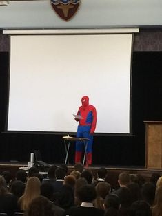 a man in a red and blue suit is standing on a stage with a projector screen behind him