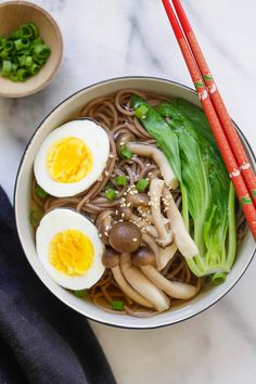 a bowl filled with noodles and vegetables next to chopsticks on a marble surface