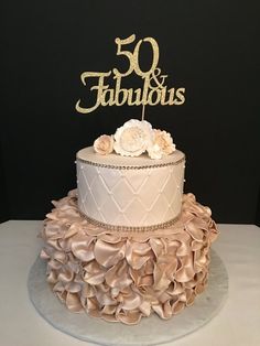 a 50th birthday cake decorated with ruffles and a gold 50 fabulous sign on top