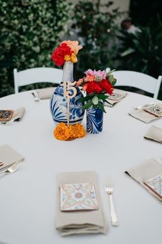 a white table topped with blue vases filled with red and yellow flowers next to silverware