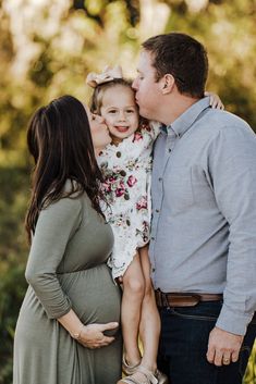 a pregnant woman kissing her husband's belly while he kisses his daughter on the cheek