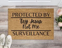 a door mat with the words protected by jesus not me surveillance on it next to shoes and flowers