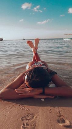 a woman laying on top of a sandy beach next to the ocean with her feet in the water