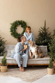 a man and woman sitting on a couch with a dog in front of christmas trees