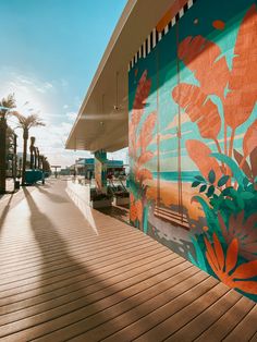 a mural on the side of a building next to a boardwalk with benches and palm trees