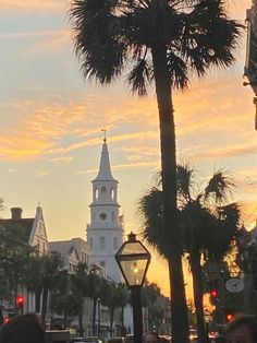 people are walking down the street in front of palm trees and a white church steeple