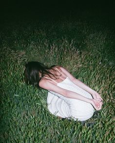 a woman is sitting in the grass with her hands on her knees and eyes closed