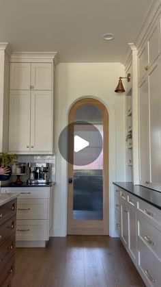 a kitchen with white cabinets and wood floors, an arched glass door leads to the dining room