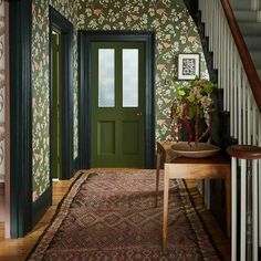 an entryway with green door and floral wallpaper on the walls next to stairs