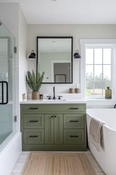 a bathroom with green cabinets and a white bathtub next to a large mirror on the wall