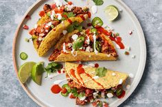 three tacos on a plate with lime wedges