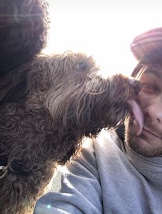 a man is kissing his dog on the nose with sun shining in the back ground