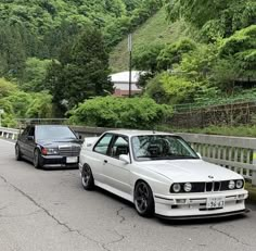 two cars parked next to each other on the side of a road with trees in the background