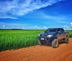 a truck parked on the side of a dirt road in front of a green field