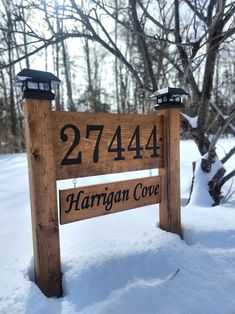 a wooden sign sitting in the snow next to some trees and bushes with numbers on it