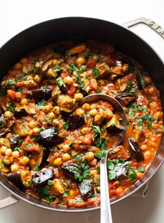 a pan filled with stew and vegetables on top of a white counter next to a spoon