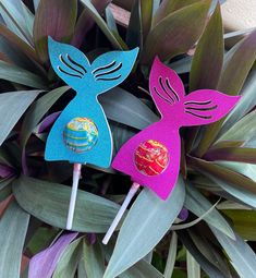 two paper mermaid lollipops sitting on top of green leaves