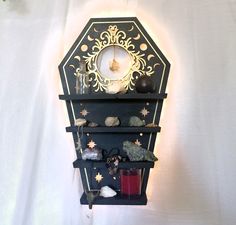 a wall mounted shelf with candles, rocks and other items on it in front of a white background