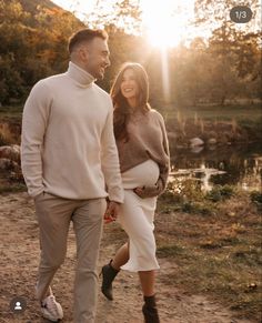 a man and woman walking down a path holding hands while the sun is setting behind them