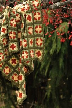 a crocheted blanket hanging from a tree branch with red berries in the background