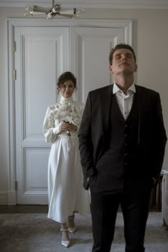 a man standing next to a woman in a white dress and black suit with her eyes closed