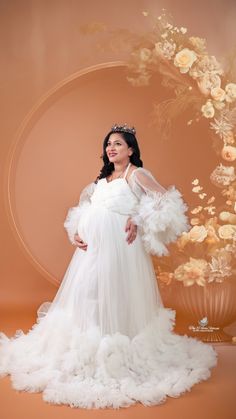 a pregnant woman in a white gown with feathers on her belly, posing for the camera