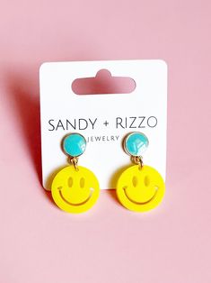 a pair of yellow smiley face earrings on a pink background