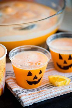 three cups filled with liquid and decorated pumpkin faces