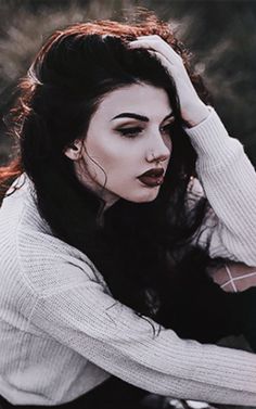 a woman sitting on the ground with her hands in her hair and wearing a white sweater