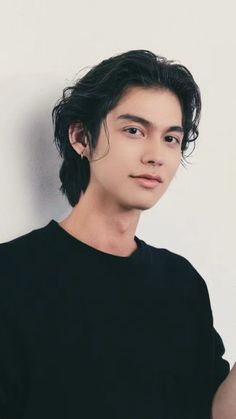 a young man with black hair is leaning against a white wall