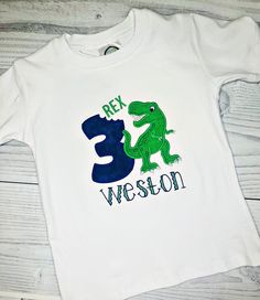 a white t - shirt with a green and blue dinosaur on the front that says rex, welson