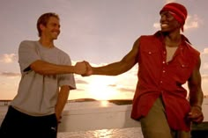 two men holding hands while standing next to each other on a boat in the water