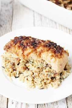 a white plate topped with rice and meat covered in sauce next to a casserole dish