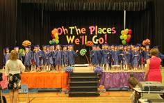 a group of people standing on top of a stage in front of a sign that says oh the places we'll go